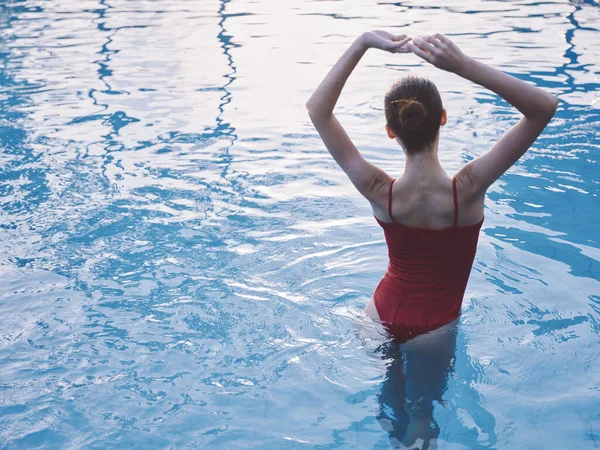 Sexy mujer en traje de baño rojo sostiene sus manos por encima de su cabeza en la piscina vista trasera —  Fotos de Stock
