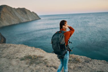 Deniz manzarası yakınındaki dağlarda sırt çantalı, kırmızı kazaklı bir gezgin.