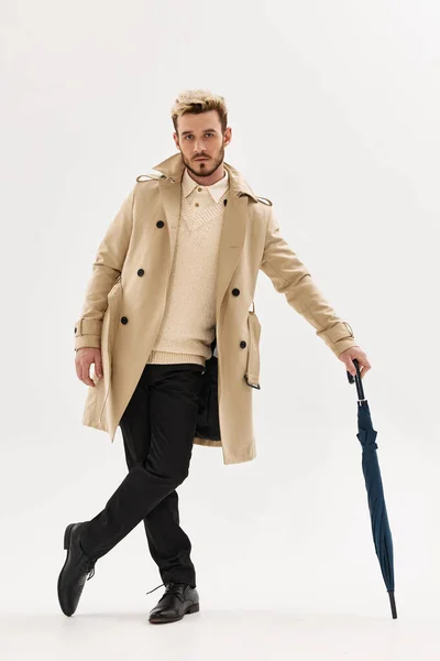 Людина в бежевому пальто парасолька в руках позує стиль життя легкий фон — стокове фото