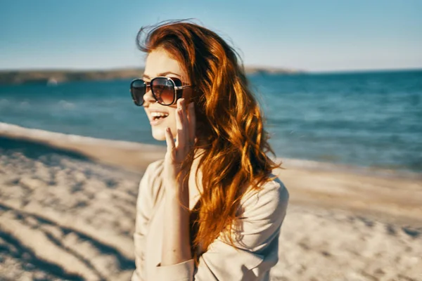 Vista laterale della donna dai capelli rossi modello in camicia e occhiali vicino al mare sulla spiaggia — Foto Stock