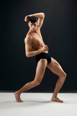 Siyah külotlu çıplak kaslı yakışıklı adam stüdyoda poz veriyor.