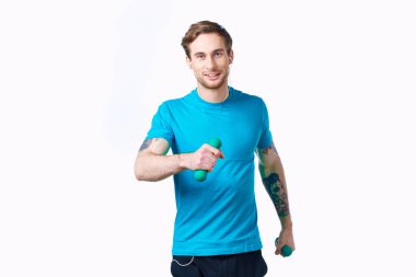 Elinde dambıllar olan mavi tişörtlü bir sporcu spor salonu dövmesi yaptırıyor.