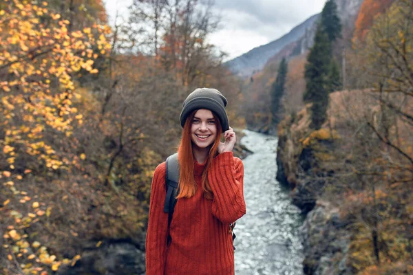 Sırt çantalı bir kadın dağlarda nehir kenarında yürüyüş yapıyor.