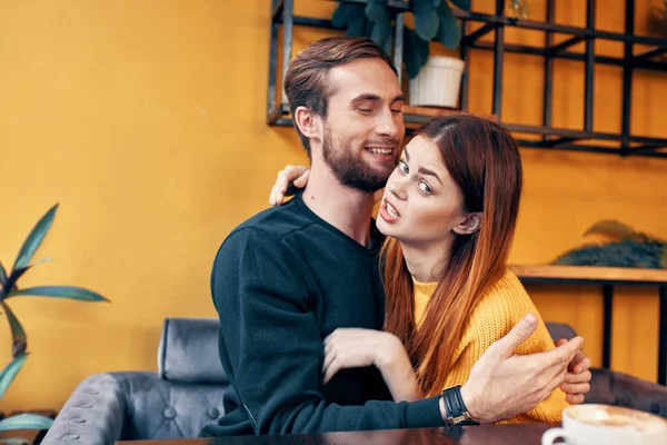Νέοι ερωτευμένοι αγκαλιάζονται ενώ κάθονται σε ένα τραπέζι σε ένα καφέ και πορτοκαλί τοίχο εσωτερικό — Φωτογραφία Αρχείου