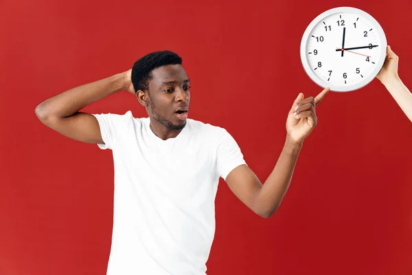 Homme apparence africaine en blanc t-shirt horloge studio fond rouge — Photo