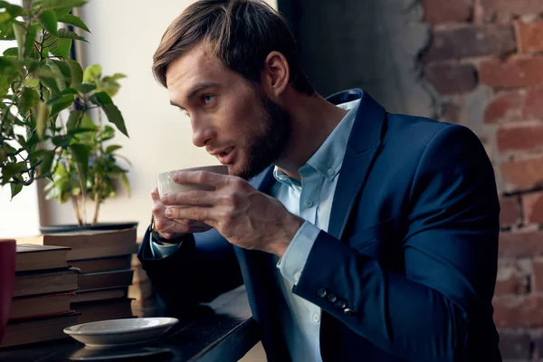 Un homme en costume boit du café près de la fenêtre d'un café. — Photo