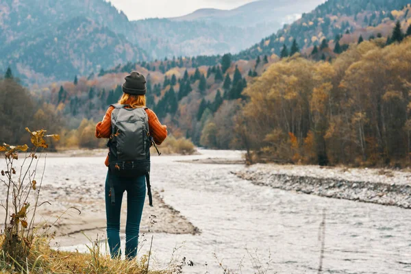 Mujer en jeans y una chaqueta con una mochila cerca del río en las montañas paisaje naturaleza —  Fotos de Stock