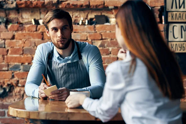 Un uomo con una tazza di caffè e tutti i grembiuli a un tavolo da caffè e una donna in camicia e gonna rossa vista ritagliata — Foto Stock