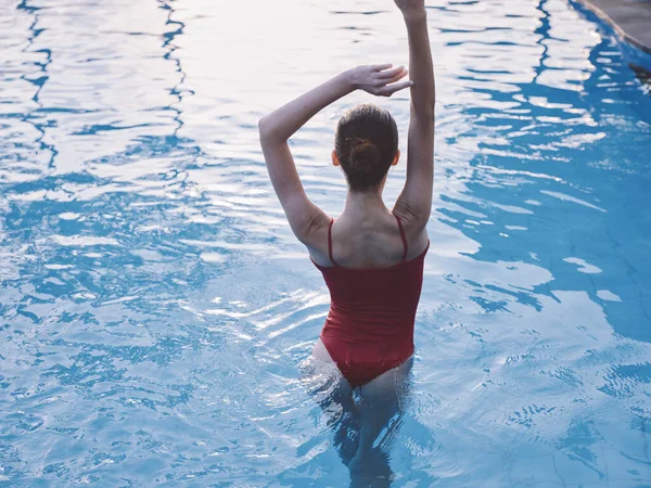 Sexy mujer con los brazos levantados de pie en la piscina en un traje de baño rojo vista trasera —  Fotos de Stock
