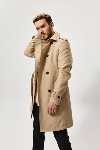 Een blonde man in een beige jas en in een donkere broek op een lichte achtergrond — Stockfoto