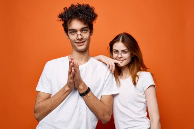 Beyaz tişörtlü ve gözlüklü genç çift eğlenceli moda turuncu arka plan