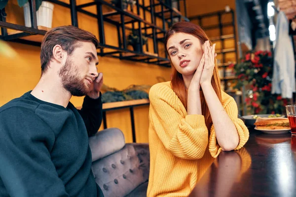 Mężczyzna mówi coś młodej kobiecie w swetrze przy stole w kawiarni komunikacji przyjaciół — Zdjęcie stockowe