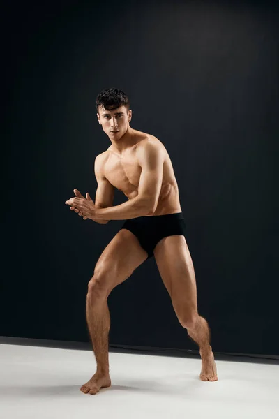 Full-délka sportovní muž s svalnatým tělem v černé kalhotky pózovat na tmavém pozadí — Stock fotografie