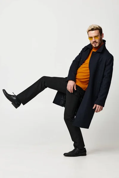 Modny mężczyzna w płaszczu pomarańczowy sweter i spodnie podniósł nogę w górę widok z boku — Zdjęcie stockowe
