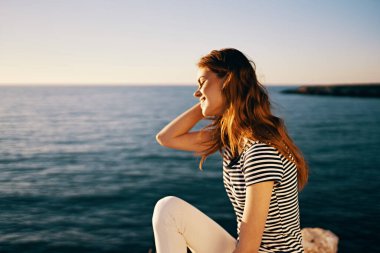 Tişörtlü ve beyaz pantolonlu bir kadın deniz batımını resmediyor.