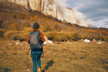 Kadın sonbaharda doğada dinleniyor dağlarda mavi gökyüzü manzarası sırt çantası