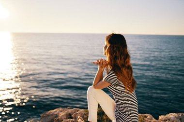 Denizin kıyısındaki sahilde oturan ve gün batımını izleyen bir kadın.