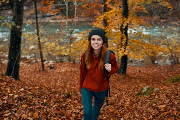 Un voyageur en pull rouge et un chapeau se promène dans la forêt d'automne près d'une rivière de montagne vue de dessus — Photo