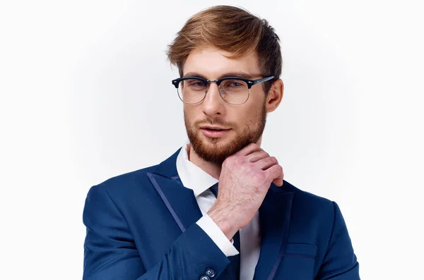 Hombre de negocios en un traje y gafas sostiene su mano cerca de su cara en un fondo claro chaqueta azul corbata clásico — Foto de Stock