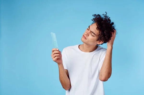 Homem bonito com cabelo encaracolado segurando pente na mão e fundo azul corte vista — Fotografia de Stock