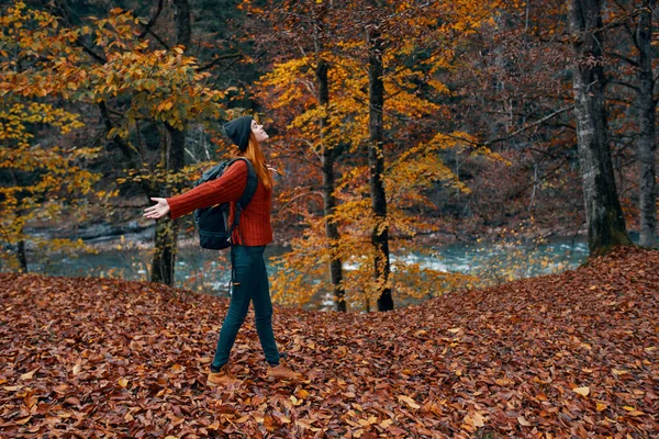 Gevallen bladeren in het park in de herfst en de rivier op de achtergrond vrouw toerist met een rugzak reizen — Stockfoto