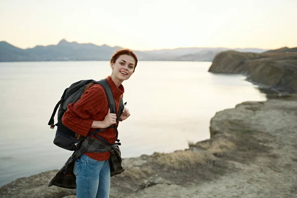 Donna al tramonto vicino al mare in montagna con uno zaino sulle spalle — Foto Stock