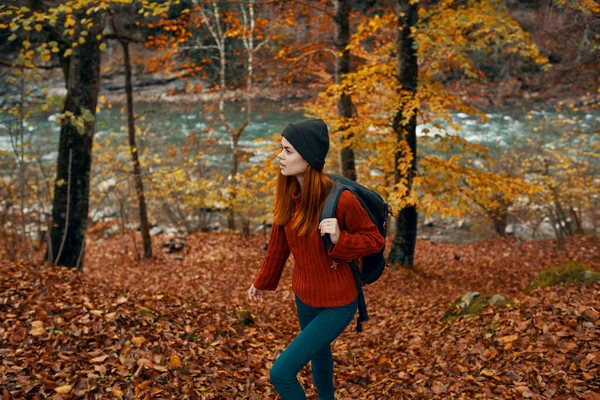 Vrouw in een trui met een rugzak rustend in een park bij de rivier in de natuur in de herfst — Stockfoto