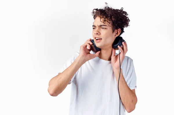 Emotionaler Typ mit lockigem Haar im Kopfhörer hört Musik auf hellem Hintergrund — Stockfoto
