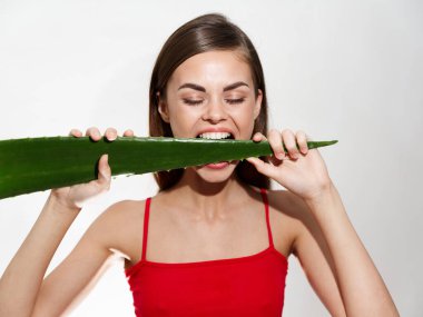Beyaz dişli duygusal bir kadın arka planda bir aloe yaprağını kemiriyor.