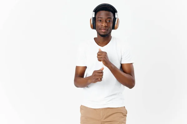 Man i en vit t-shirt med hörlurar lyssnar på musik ljus bakgrund — Stockfoto