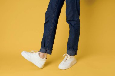 Beyaz spor ayakkabılı kadın bacakları sarı arka plan tarzı poz veriyor.