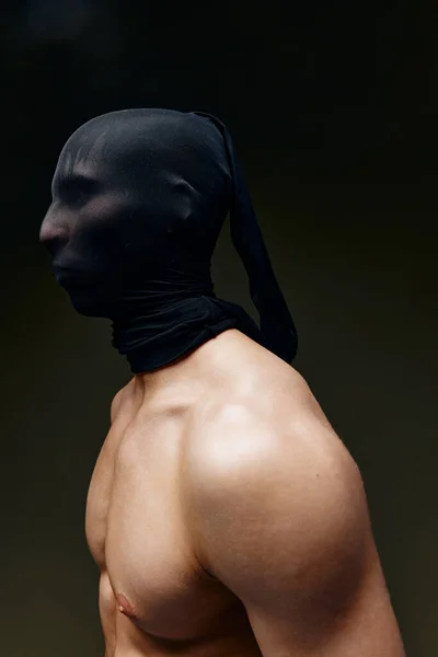 Hombre con máscara negra en su cara y bombeado los músculos del brazo culturista Aptitud fondo oscuro —  Fotos de Stock