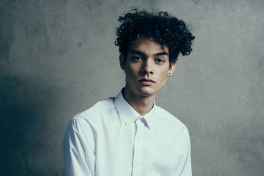 Yakışıklı, kıvırcık saçlı, beyaz gömlekli, modern görünüyor.