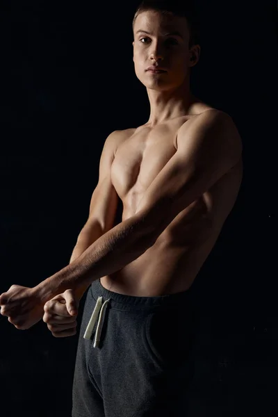 Культурист в спортивних штанах з голим торсом на чорному фоні жестикулює руками — стокове фото