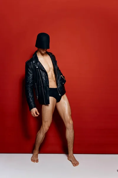 Attraente uomo con un torso nudo e in mutandine nere giacca di pelle maschera nera sulla testa sfondo rosso — Foto Stock