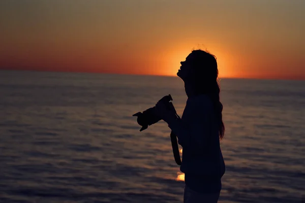 Nő naplementekor közel a tengerhez egy fényképezőgéppel a kezében — Stock Fotó