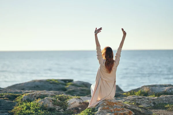 Žena ve svetru gesta s rukama nad hlavou v horách v blízkosti moře čerstvý vzduch — Stock fotografie