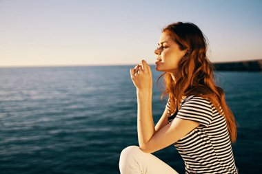 Gün batımında gezgin deniz manzaralı bir kayanın üzerinde oturuyor.