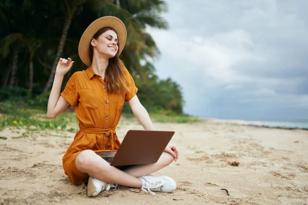 해변에서 노트북 여행을 하며 모래 위에 앉아 있는 여성 도보 여행자 — 스톡 사진