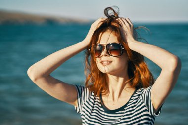 Deniz kenarındaki kumsalda bir yaz gezgini elleriyle kafasına dokunuyor.