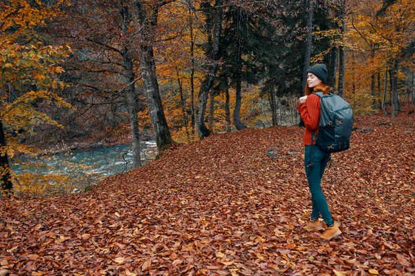 Femme en automne dans le parc avec des feuilles tombées et un sac à dos sur son dos rivière en arrière-plan — Photo