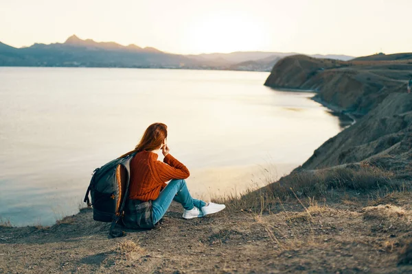 Woman hiker with backpack in the mountains at sunset near the sea — Stock Photo, Image