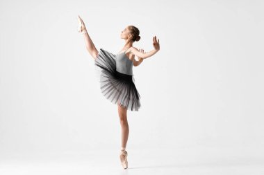 Ballerina in pointe shoes and a tutu is dancing on a light background standing on tiptoes