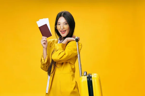 Happy woman in jacket and suitcase holding passport for travel on yellow background — Φωτογραφία Αρχείου