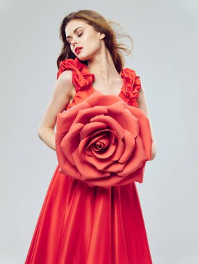 portrait of a woman in a red dress with a decorative flower in her hand on a light background cropped view