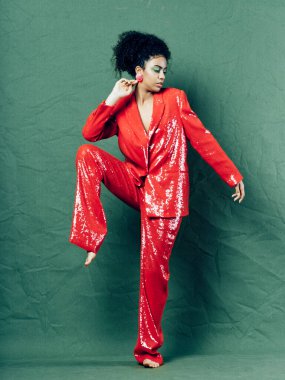 fashionable woman in red suit lifted her leg up and dances on green background indoors