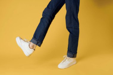 Kadın ayakları kırpılmış beyaz ayakkabılar, sarı arka plan.