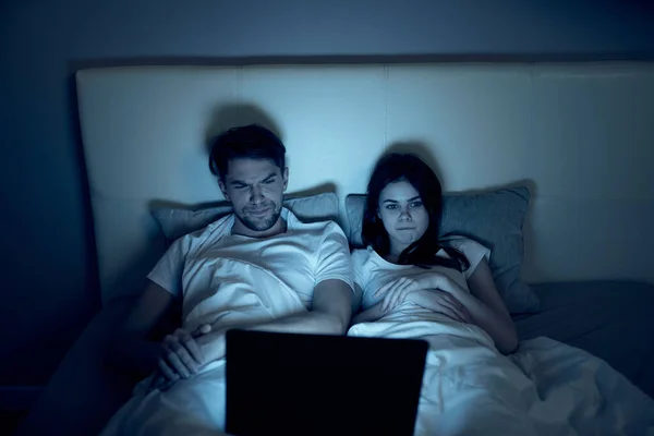 Młoda para leżąca w nocy na łóżku przed laptopem — Zdjęcie stockowe