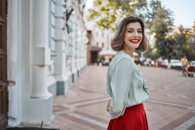 Kırmızı dudaklı tatlı sarışın kız binanın yanında yürüyor.