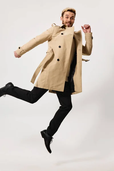 Человек в бежевом пальто осенний стиль прыгать студия легкий фон — стоковое фото